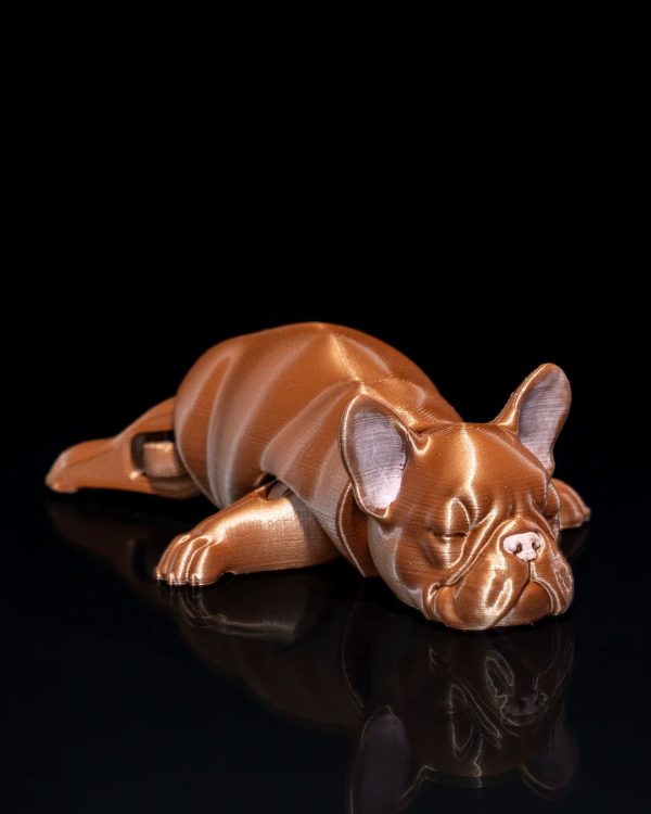 Articulated 3D printed English Bulldog figure in a lying position with a shiny bronze finish, displayed against a black background.
